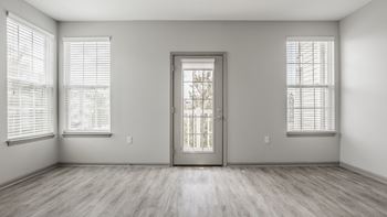A room with plank flooring and a large window with blinds